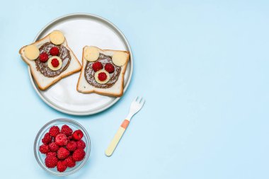 Komik ayı suratlı tost ekmeği. Fıstık ezmeli, peynirli ve ahududu tabakta mavi arka plan fotokopi alanı. Çocuklar tatlı tatlı tatlı kahvaltı öğle yemeği.