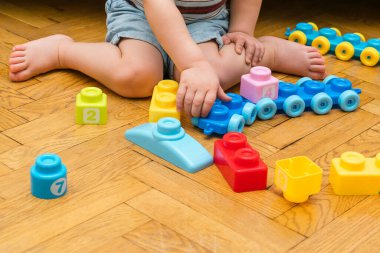 Evde çok renkli inşaatçıyla oynayan sevimli beyaz bir çocuk var. Bebek elleri plastik bloklardan kule yapıyor. Çocuk mantığı geliştirme ve çocuk yuvası, anaokulu kavramı.