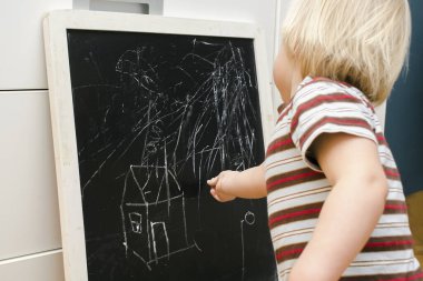 Küçük sevimli beyaz çocuk evdeki tahtaya tebeşir çiziyor. Bebek eli boyama. Çocuklar için yaratıcı kapalı alan aktivitesi, gelişim, çocuk yuvası, anaokulu konsepti.