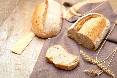 Bir somun taze ekmek ve ahşap arka planda kesilmiş baget ekmeği, fotokopi alanı, fırında pişirilmiş hamur işi yakın plan..