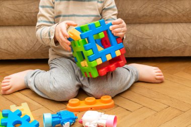 Evde çok renkli inşaatçıyla oynayan sevimli beyaz bir çocuk var. Bebek elleri plastik bloklardan kule yapıyor. Çocuk mantığı geliştirme ve çocuk yuvası, anaokulu kavramı.