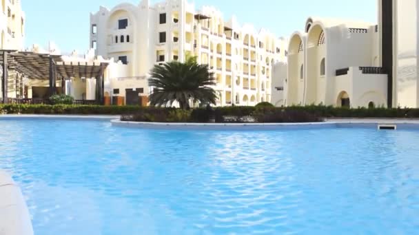 Piscina com água azul clara em movimento, pequena ondulação ondulação, no resort do hotel no dia ensolarado quente ao ar livre. Verão conceito de férias recreativas tropicais, Egito Hurghada, vídeo de filmagens — Vídeo de Stock