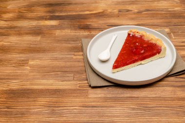 Lezzetli kırmızı klasik cheesecake, ahşap kırsal arka planda jöleli tatlı dilimi. Tatlı çatalıyla servis edilen seramik tabakta lezzetli bir pasta ve fotokopi alanı olan peçete..