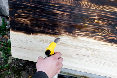 Erkek eller ahşap masayı yakıyor, masa, ocaklı yüzey, dışarıda odun yakan el işi. Balonla gaz ocağını tutan ve arka bahçede ateş yakan adamı kapatın..