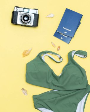 Seyahat tatili yatakları, aksesuar eşyaları, şapka, pasaport, güneş gözlüğü, kıyafetler, mayo, kamera, sarı arka planda deniz kabuğu, planlama macerası.