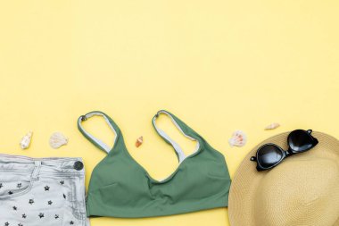 Seyahat tatili yatakları, aksesuar eşyaları, şapka, güneş gözlükleri, kıyafetler, mayo, sarı arka planda fotokopi alanı olan deniz kabukları, planlama macerası.