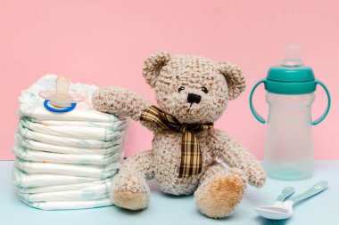 Oyuncak ayıyla bebek bezi yığını, masada bir şişe süt. Bebek için yeni doğmuş bir kız çocuğu, hediye olarak mavi pembe arka planda hediye. Sağlık sigortası, hijyen konsepti.