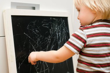 Küçük sevimli beyaz çocuk evdeki tahtaya tebeşir çiziyor. Bebek eli boyama. Çocuklar için yaratıcı kapalı alan aktivitesi, gelişim, çocuk yuvası, anaokulu konsepti.