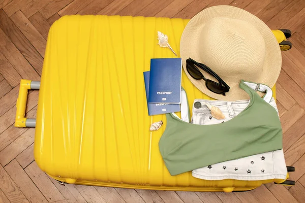 Seyahat yeri, seyahat aksesuarları, yaz şapkası, pasaport, güneş gözlüğü, kıyafet, mayo, fotokopi alanı olan sarı bavuldaki kamera, planlama macerası..