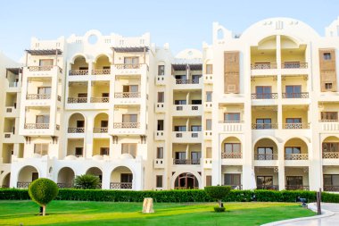 Lüks lüks, modern apartman tipi otel cephesi, sıcak güneşli bir günde yeşil çimenli tropikal tatil köyü. Yaz tropikleri Mısır 'da tatil, kaçış konsepti.