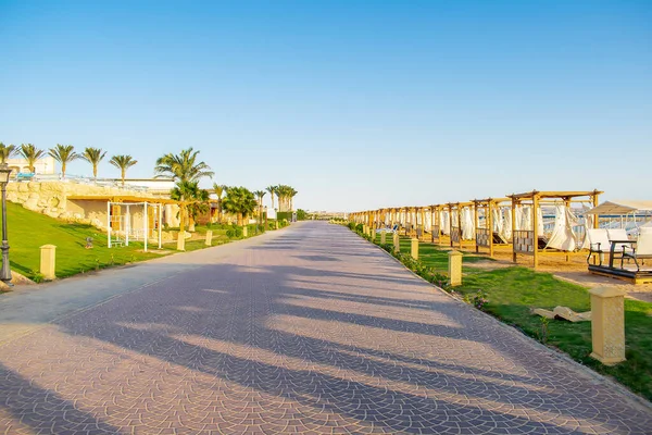 Road along lots of wooden furniture for rest, deck chair bed, gazebo on sand beach with curtains, tropical sea luxury resort.Summer vacation on warm sunny day outdoor in sunshine, sunlight.