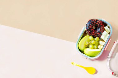 Depoda, donutlu, elmalı, üzümlü ve bej arka planda muzlu yemek servisi. Sağlıklı dengeli beslenme, beslenme çantası paket paket paket hazır..