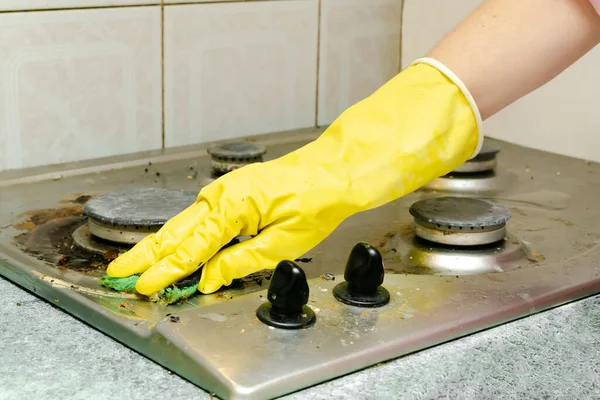 Cleaning dirty gas stove from grease, food leftovers deposits. woman\'s hand in protective glove with sponge rag and detergent washing kitchen stove. home cleaning service concept.