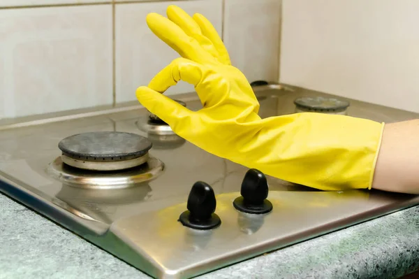 Cleaning dirty gas stove from grease, food leftovers deposits. woman's hand in protective glove washing kitchen stove. home cleaning service concept.