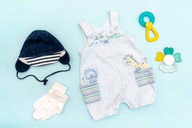 Şirin bebek tulumları, mayo, şapka, oyuncaklı çoraplar, bağcıklar. Çocuklar, çocuk giysileri ve mavi renkli aksesuarlar. Yeni doğan, bebek modası, kıyafet. Düz yatış, üst görünüm.