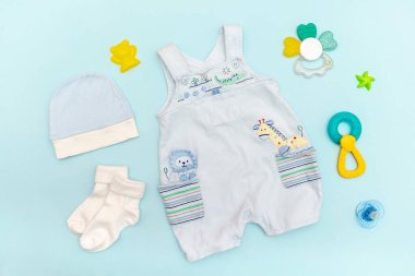 Şirin bebek tulumları, mayo, şapka, oyuncaklı çoraplar, bağcıklar. Çocuklar, çocuk giysileri ve mavi renkli aksesuarlar. Yeni doğan, bebek modası, kıyafet. Düz yatış, üst görünüm.