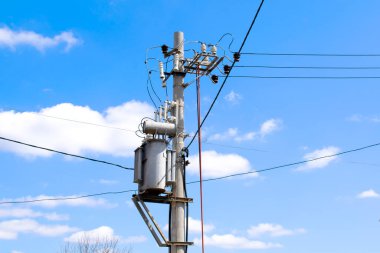 Yüksek elektrik gerilim kabloları ve direk elektrik hatları, elektrik kuleleri, elektrik trafosu, parlak mavi gökyüzüne karşı, bulutlar ve güneş. Uzun mesafelerde elektrik transferi.
