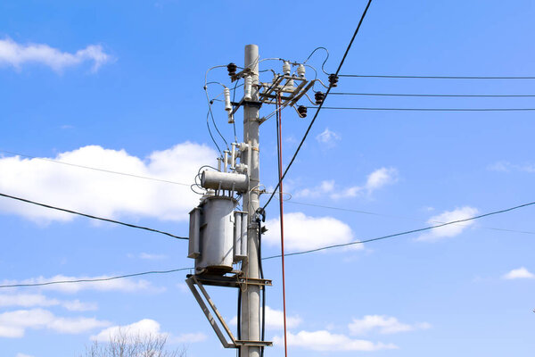 High Electric voltage wires and pole power lines,electric towers,power transformer against vibrant blue sky, clouds and sun. Transmission of electricity on long distances.