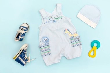 Şirin bebek tulumları, mayo, şapka, oyuncaklı spor ayakkabılar, bağcıklar. Çocuklar, çocuk giysileri ve mavi renkli aksesuarlar. Yeni doğan, bebek modası, kıyafet. Düz yatış, üst görünüm