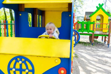 Tatlı, komik, sarışın, küçük çocuk. Oyuncak arabada, otobüste, çocuk parkında oturuyor. Çocuklar fiziksel, duygusal gelişim ve çocukluk bakımı, anaokulu kavramı..