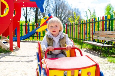 Şirin, komik, sarışın, küçük çocuk. Oyuncak arabada oturuyor, araba sürüyor. Çocuklar, fiziksel, duygusal gelişim ve çocukluk bakımı, anaokulu kavramı..