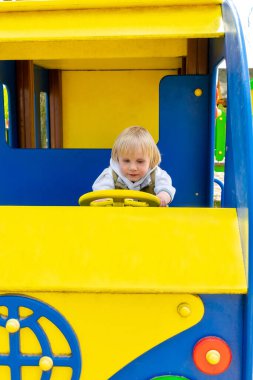 Tatlı, komik, sarışın, küçük çocuk. Oyuncak arabada, otobüste, çocuk parkında oturuyor. Çocuklar fiziksel, duygusal gelişim ve çocukluk bakımı, anaokulu kavramı..