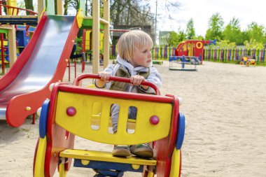 Şirin, komik, sarışın, küçük çocuk. Oyuncak arabada oturuyor, araba sürüyor. Çocuklar, fiziksel, duygusal gelişim ve çocukluk bakımı, anaokulu kavramı..