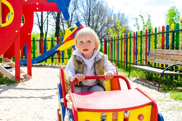 Şirin, komik, sarışın, küçük çocuk. Oyuncak arabada oturuyor, araba sürüyor. Çocuklar, fiziksel, duygusal gelişim ve çocukluk bakımı, anaokulu kavramı..