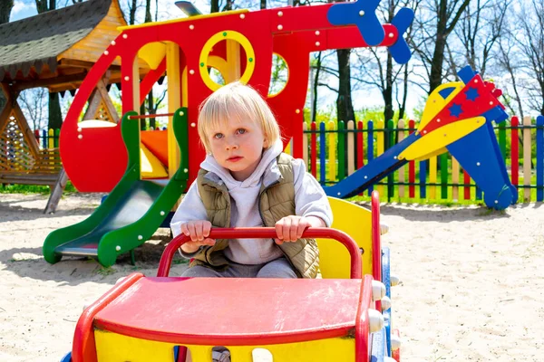 Şirin, komik, sarışın, küçük çocuk. Oyuncak arabada oturuyor, araba sürüyor. Çocuklar, fiziksel, duygusal gelişim ve çocukluk bakımı, anaokulu kavramı..