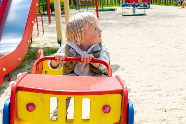 Şirin, komik, sarışın, küçük çocuk. Oyuncak arabada oturuyor, araba sürüyor. Çocuklar, fiziksel, duygusal gelişim ve çocukluk bakımı, anaokulu kavramı..