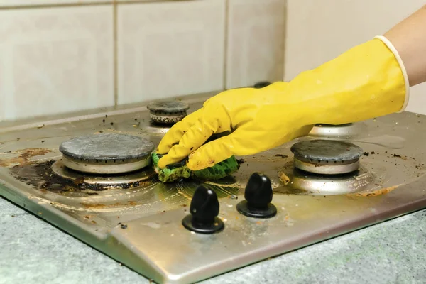 Cleaning dirty gas stove from grease, food leftovers deposits. woman\'s hand in protective glove with sponge rag and detergent washing kitchen stove. home cleaning service concept.