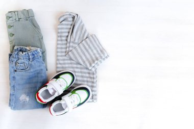Spor ayakkabılı kazak ve kot pantolon. Beyaz arka planda bahar, sonbahar ya da yaz için bebek kıyafetleri ve aksesuarlar. Moda çocuk kıyafeti. Düz yatıyordu, üstten, yukarıdan..