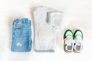 Spor ayakkabılı kazak ve kot pantolon. Beyaz arka planda bahar, sonbahar ya da yaz için bebek kıyafetleri ve aksesuarlar. Moda çocuk kıyafeti. Düz yatıyordu, üstten, yukarıdan..