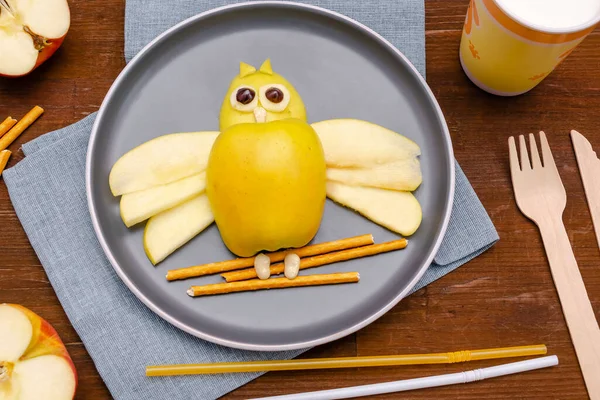 Funny owl face shape snack with apple, wheat crispy bread straw on plate,milk in glass. Cute kids childrens baby\'s sweet dessert, healthy breakfast,lunch, food art on wooden background,top view.