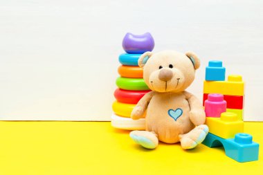 Renkli piramit, inşaatçı, çocuklar için oyuncak blokları beyaz sarı arka planda oynayan oyuncak ayı, bebeğin çocukluk gelişimi, küçük çocuğun konsepti için eğitici mantık oyuncakları, kopyalama alanı.