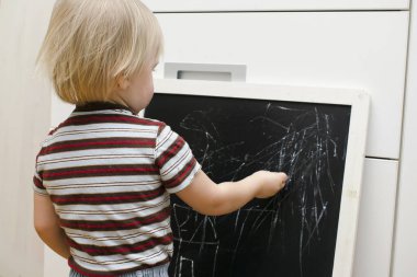 Küçük sevimli beyaz çocuk evdeki tahtaya tebeşir çiziyor. Bebek eli boyama. Çocuklar için yaratıcı kapalı alan aktivitesi, gelişim, çocuk yuvası, anaokulu konsepti.