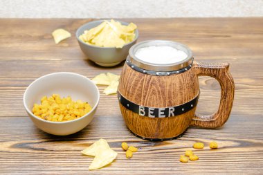 Kahverengi bardak bira köpüklü ve çıtır çıtır atıştırmalıklar, krakerler, krakerler, cipsler, fındıklar ahşap masada, arka plan yakın. Alkol kokteyli, bar partisi konsepti..