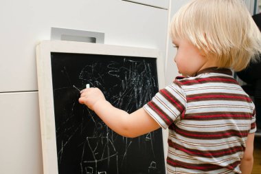 Küçük sevimli beyaz çocuk evdeki tahtaya tebeşir çiziyor. Bebek eli boyama. Çocuklar için yaratıcı kapalı alan aktivitesi, gelişim, çocuk yuvası, anaokulu konsepti.