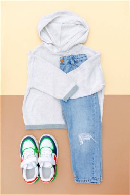 Spor ayakkabılı kazak ve kot pantolon. Bahar, sonbahar ya da yaz için bej rengi kahverengi arka planda bebek kıyafetleri ve aksesuarlar. Moda çocuk kıyafeti. Düz yatıyordu, üstten, yukarıdan..