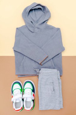 Kazak ve spor ayakkabılı gri pantolon. Bahar, sonbahar ya da yaz için bej rengi kahverengi arka planda bebek kıyafetleri ve aksesuarlar. Moda çocuk kıyafeti. Düz yatıyordu, üstten, yukarıdan..