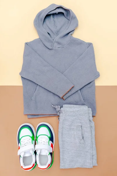 Kazak ve spor ayakkabılı gri pantolon. Bahar, sonbahar ya da yaz için bej rengi kahverengi arka planda bebek kıyafetleri ve aksesuarlar. Moda çocuk kıyafeti. Düz yatıyordu, üstten, yukarıdan..