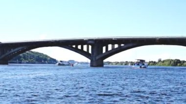 Kiev 'de güneşli bir yaz gününde mavi su ve metal yaya köprüsü olan Dnipro nehri manzaralı doğa gezisi. Nehrin içinden görüntüle, su üzerinde gemi görüntüsü..