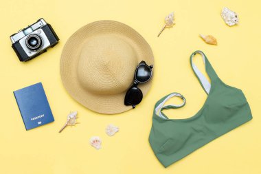 Seyahat tatili düz yatak, aksesuar nesneler, şapka, güneş gözlüğü ve kıyafetler, mayo, kamera, pasaport, deniz kabuğu sarı arka planda, planlama yolculuğu macera, yolculuk.