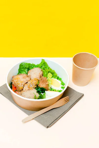 Healthy food lunch in kraft paper carton eco friendly box disposable bowl packaging container, cup on yellow background. chicken, eggs, greens. Take away delivery. environment protection, vertical.