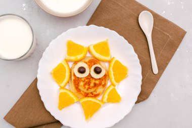 Krepten komik güneş yüzlü atıştırmalık, tabakta turuncu. Tatlı çocuklar bebeğin tatlı tatlısını, sağlıklı kahvaltısını, öğle yemeğini, sütlü ve ekşi kremalı yemek sanatını gri beton arka planda, üst manzarada.