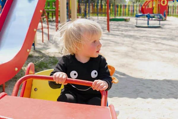 Şirin, komik, sarışın, küçük çocuk. Oyuncak arabada oturuyor, araba sürüyor. Çocuklar, fiziksel, duygusal gelişim ve çocukluk bakımı, anaokulu kavramı..