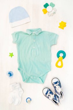 Şirin bebek tulumu, mayo, şapka, çorap, oyuncaklı spor ayakkabısı, pantolon askısı. Çocuklar, çocuk kıyafetleri ve pastel mavisi aksesuarlar. Yeni doğan, bebek modası, kıyafet. Düz yatış, üst görünüm, model.