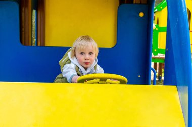 Tatlı, komik, sarışın, küçük çocuk. Oyuncak arabada, otobüste, çocuk parkında oturuyor. Çocuklar fiziksel, duygusal gelişim ve çocukluk bakımı, anaokulu kavramı..