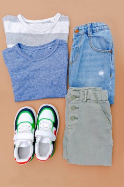 Bebek ayakkabısı, gömlek ve kot pantolon. Bahar, sonbahar ya da yaz için çocuk kıyafetleri ve aksesuarlar. Moda çocuk kıyafetleri, bej kahverengi arka planda giysiler. Düz yatıyordu, üstten, yukarıdan..