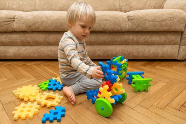 Evde çok renkli inşaatçıyla oynayan sevimli beyaz bir çocuk var. Bebek elleri plastik bloklardan kule yapıyor. Çocuk mantığı geliştirme ve çocuk yuvası, anaokulu kavramı.